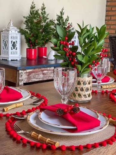 Mesa navideña con manteles individuales redondos de yute, borlas rojas y servilletas rojas