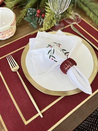 Mesa navideña con mantel individual rojo con borde dorado, plato blanco y servilleta con anillo rojo