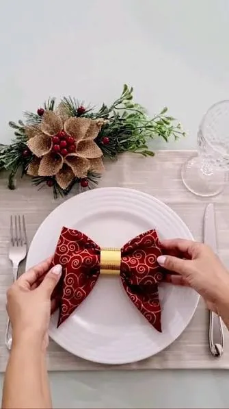 Porta-guardanapo dorado con servilleta burdeos doblada en lazo sobre mesa navideña