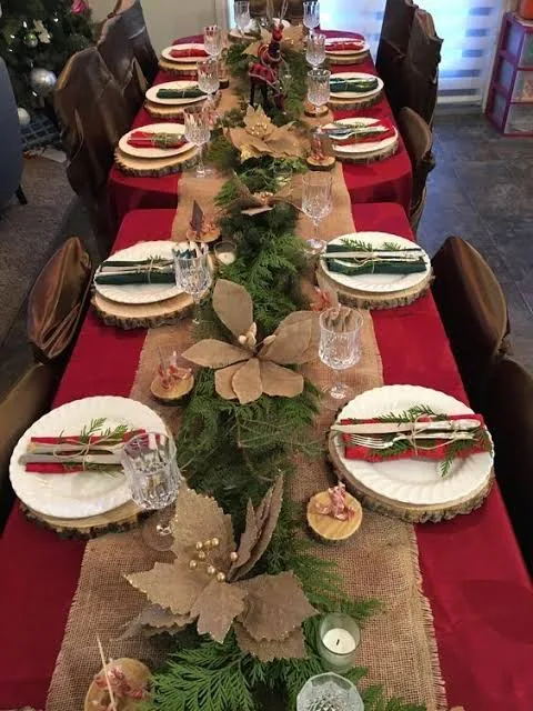 Caminho de mesa de yute sobre mantel rojo con corona de pino y flores de papel